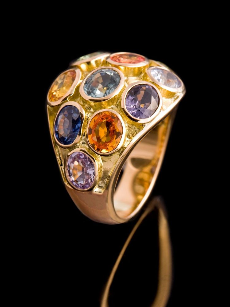 Domed gold ring set with a cluster of round sapphires in blues, violets and oranges, on black
