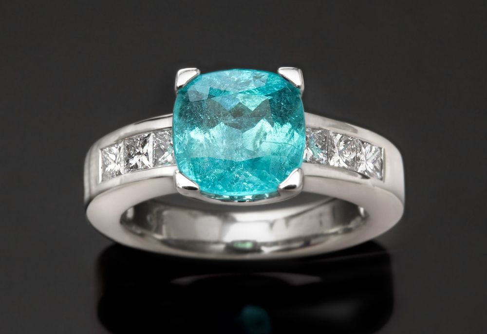A glowing Paraiba tourmaline cushion flanked by princess-cut diamonds in white gold