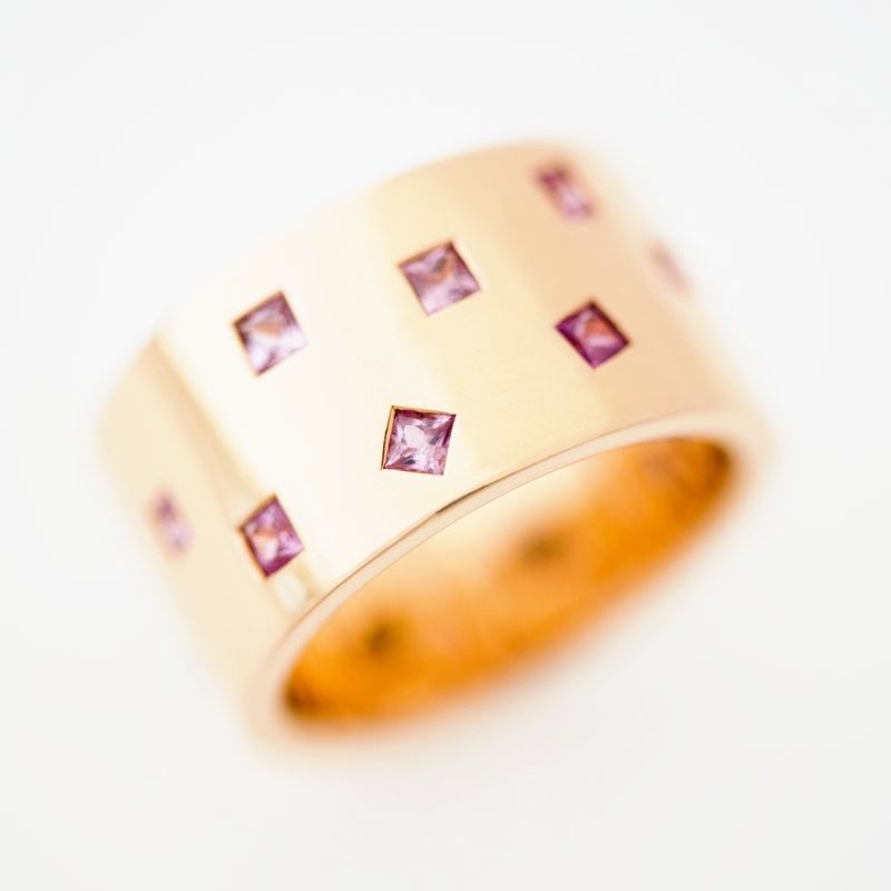 A wide polished rose gold band with square pink sapphires scattered across it