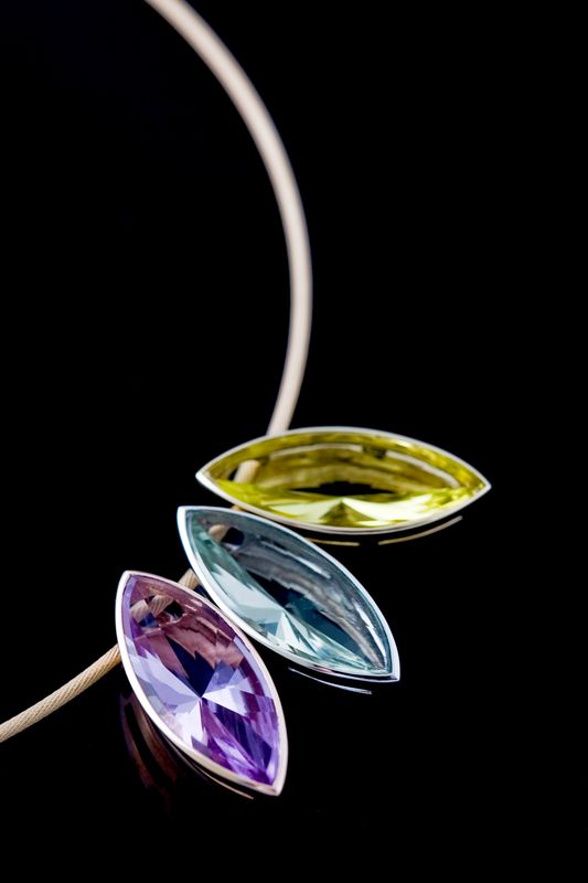 Pendant of three marquise-cut stones in green, blue and lilac hung on a gold cable, on black