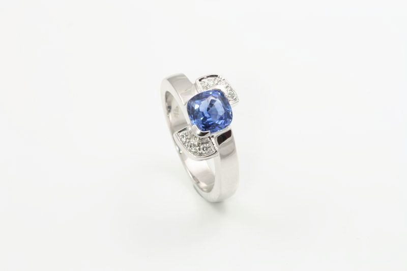 A small white gold ring with an oval blue sapphire and diamond shoulders