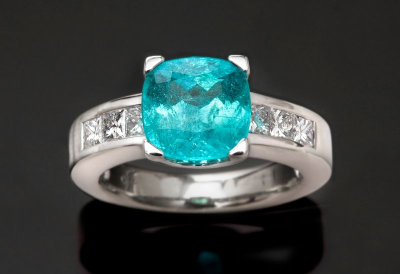 A glowing neon-blue Brazilian Paraiba tourmaline cushion flanked by channel-set princess diamonds in white gold