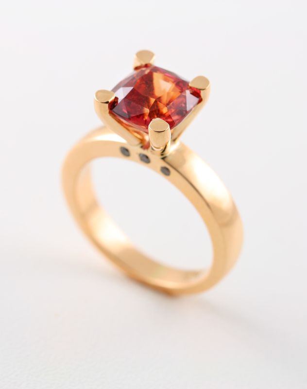 A rose gold ring with a cushion-cut orange-pink sapphire and small diamonds on the band