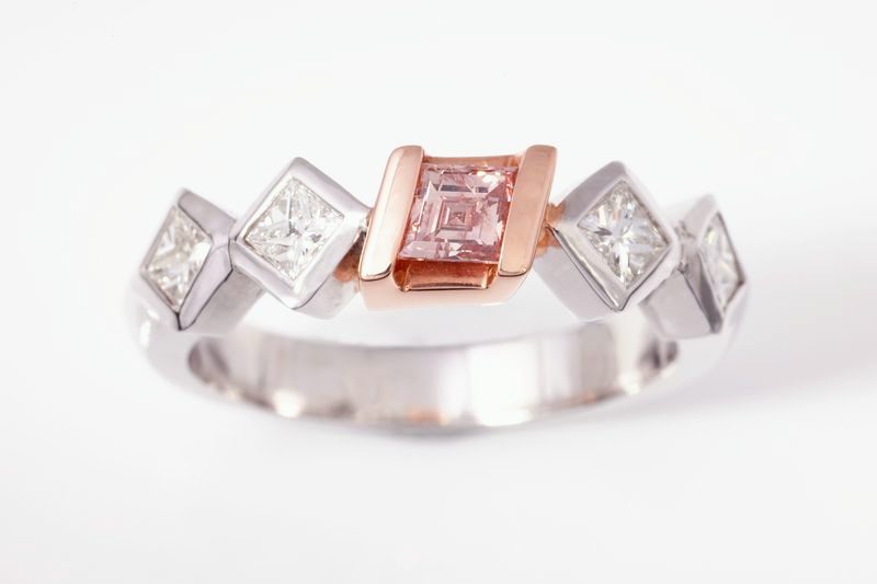 A white gold ring with a rose gold square holding a pink stone between two princess diamonds