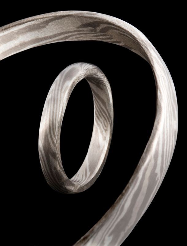 A Mokume Gane band seen edge-on, its wood-grain pattern swirling, on black