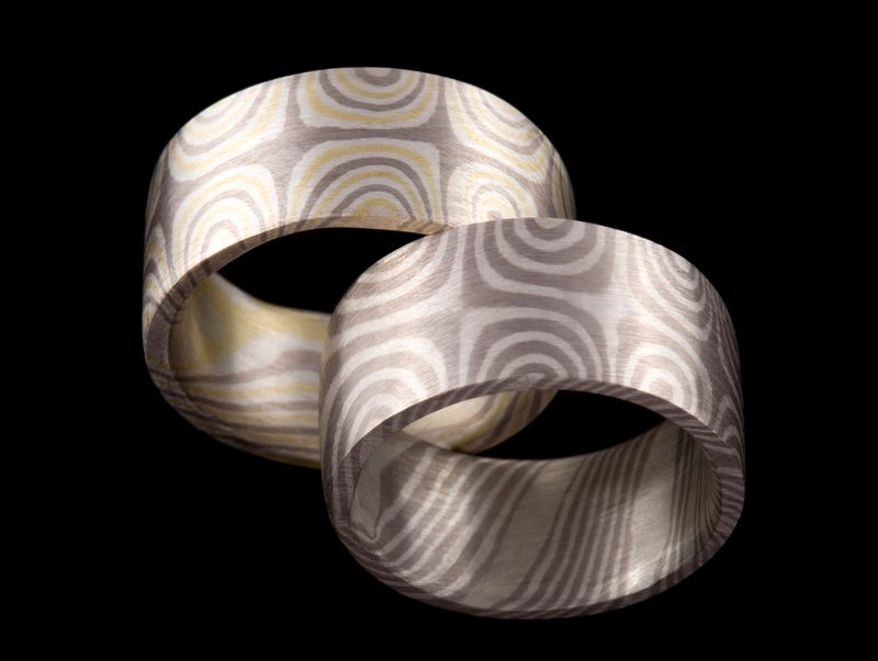 Two wide Mokume Gane bands with bold wood-grain patterning, on black