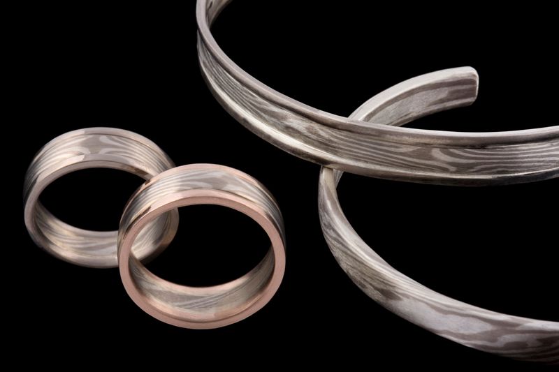 A group of Mokume Gane rings and two cuffs, on black