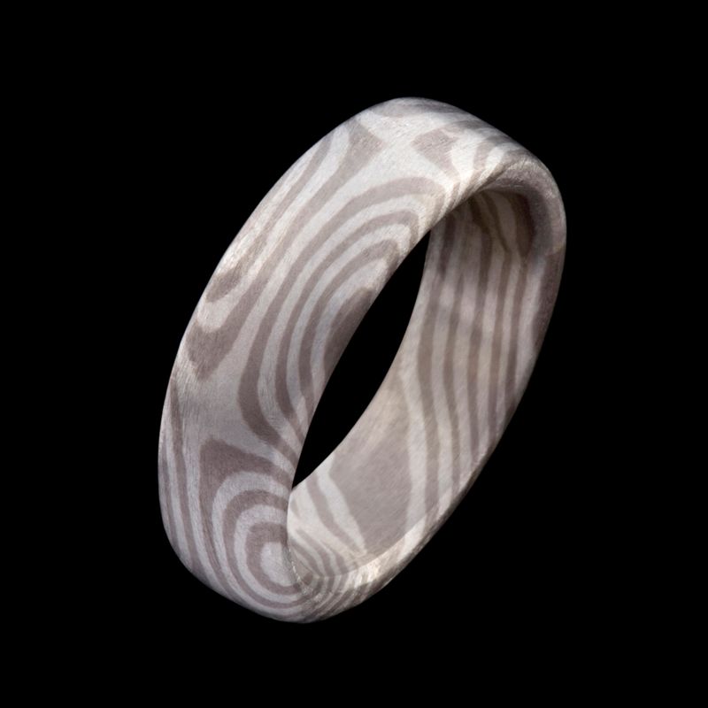 A wide Mokume Gane band, its surface patterned with pale wood-grain rings, on black