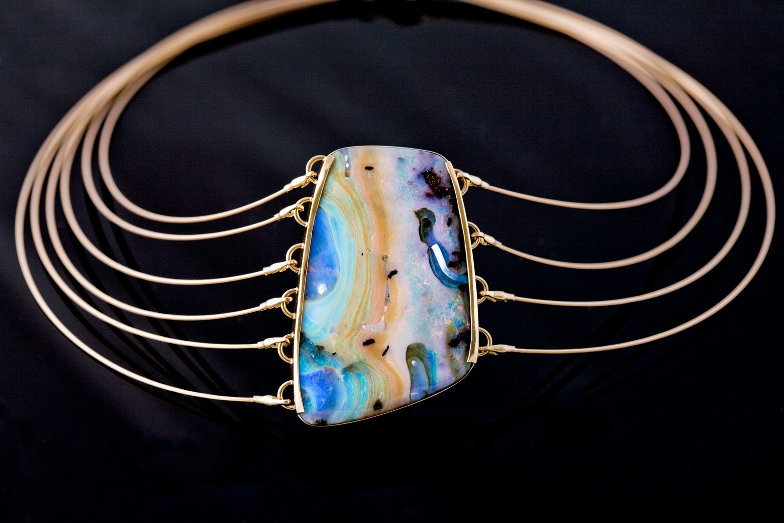 A collar of five fine gold wires fanning around a rectangular boulder opal