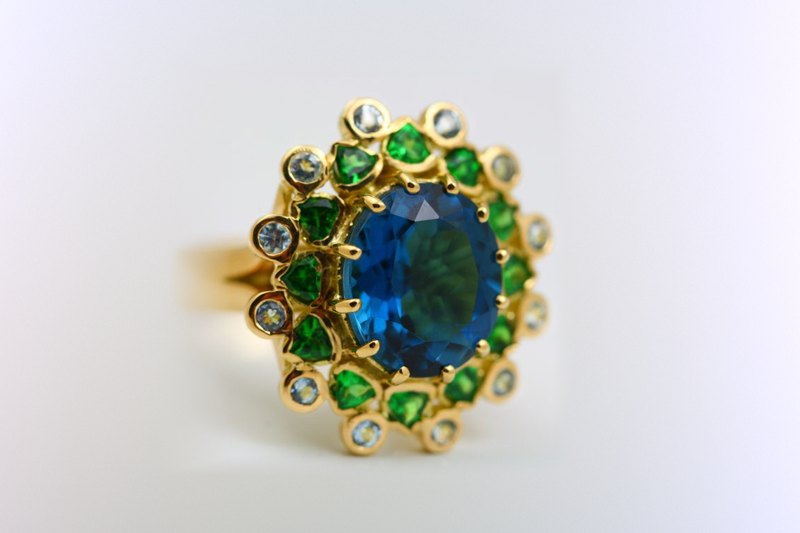London Blue Topaz halo ring: a London Blue Topaz with Tsavorites and Aquamarines in 18 karat yellow gold