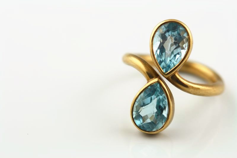 A yellow gold ring whose band crosses over to hold two pear-shaped blue topazes
