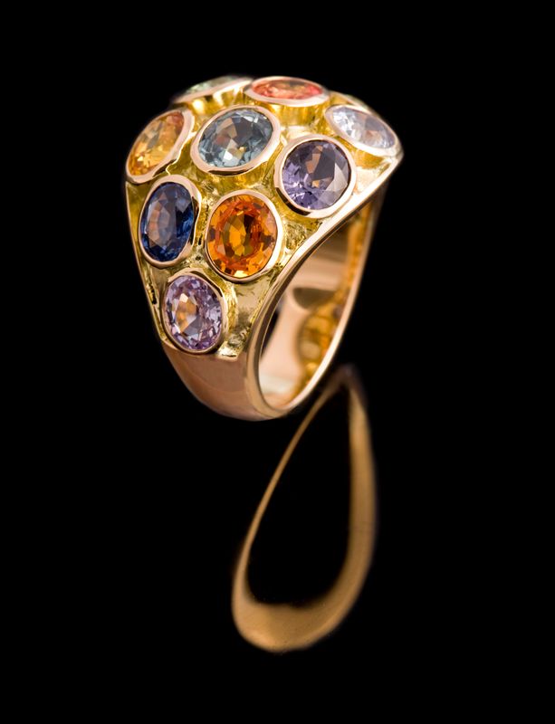 Domed gold ring set with a cluster of round sapphires in blues, violets and oranges, on black