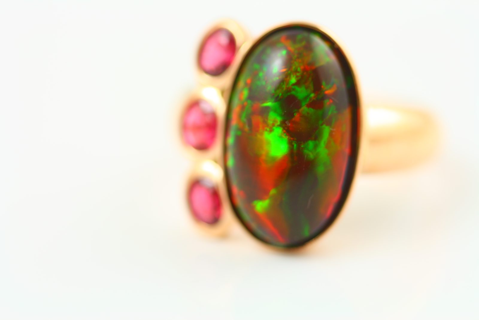 Ring with an oval black opal flashing green and orange, flanked by three round pink spinels in yellow gold